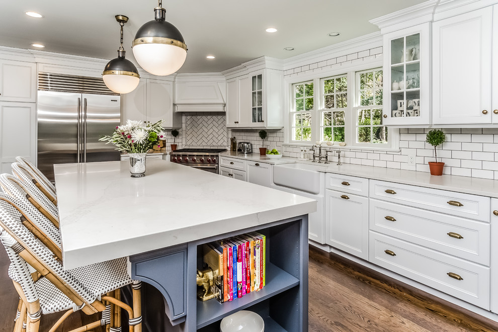 Inspiration for a large traditional l-shaped eat-in kitchen in New York with a farmhouse sink, recessed-panel cabinets, white cabinets, marble benchtops, white splashback, subway tile splashback, stainless steel appliances, dark hardwood floors, with island and brown floor.