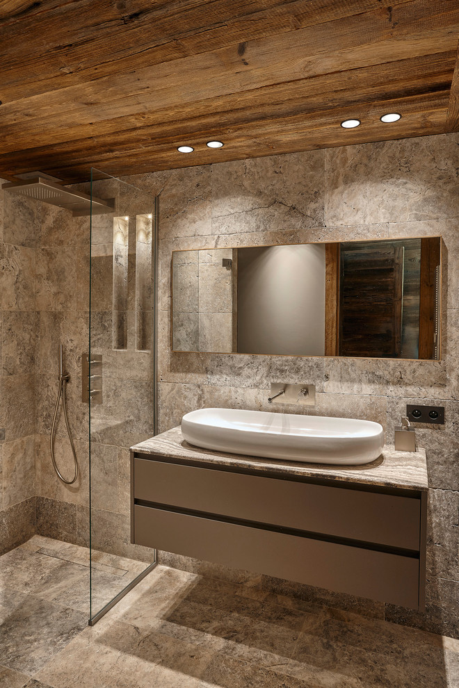 This is an example of a mid-sized country 3/4 bathroom in Lyon with grey cabinets, a curbless shower, gray tile, stone slab, travertine floors, a drop-in sink, limestone benchtops, brown walls and an open shower.