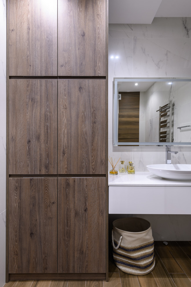 This is an example of a mid-sized transitional 3/4 bathroom in Moscow with flat-panel cabinets, white cabinets, an alcove shower, a wall-mount toilet, white tile, porcelain tile, white walls, porcelain floors, a vessel sink, solid surface benchtops, brown floor, a hinged shower door and white benchtops.