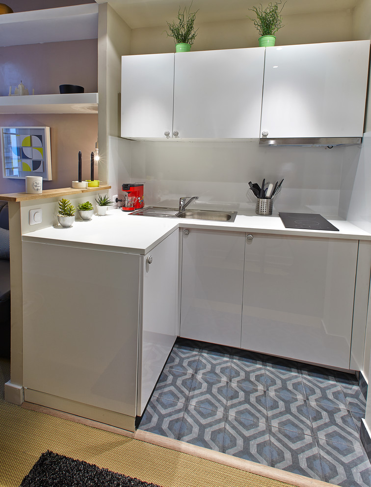 This is an example of a small modern l-shaped open plan kitchen in Paris with beaded inset cabinets, stainless steel cabinets, solid surface benchtops, white splashback, glass sheet splashback, stainless steel appliances, cement tiles, no island and multi-coloured floor.