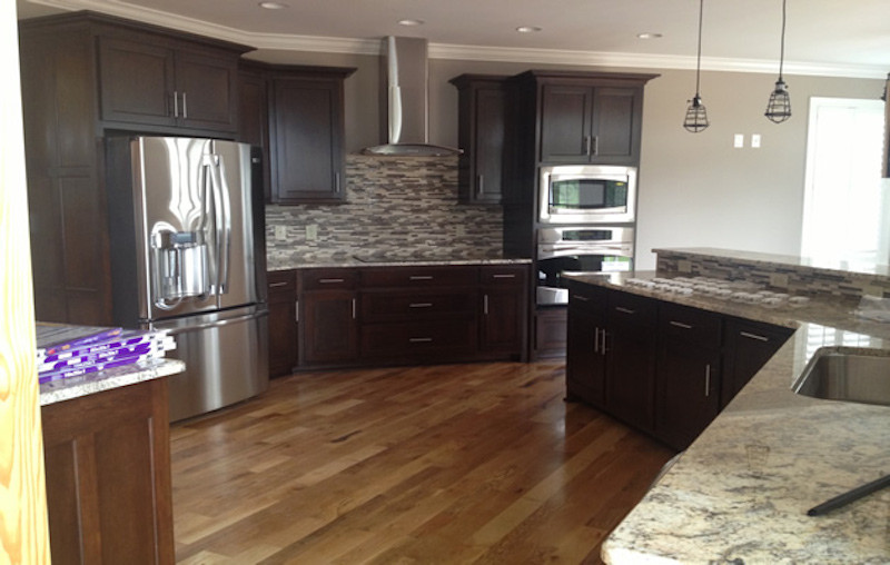 Large medium tone wood floor kitchen photo with a drop-in sink, recessed-panel cabinets, dark wood cabinets and stainless steel appliances