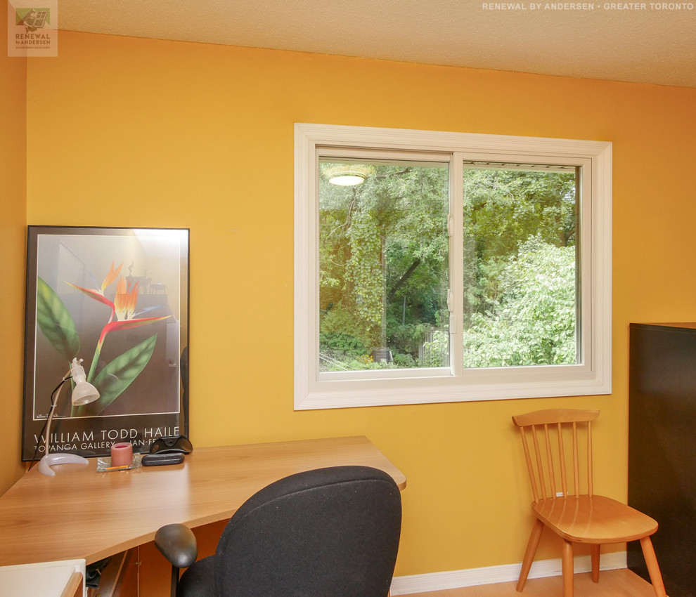 Foto på ett mellanstort arbetsrum, med gula väggar, ljust trägolv och ett fristående skrivbord