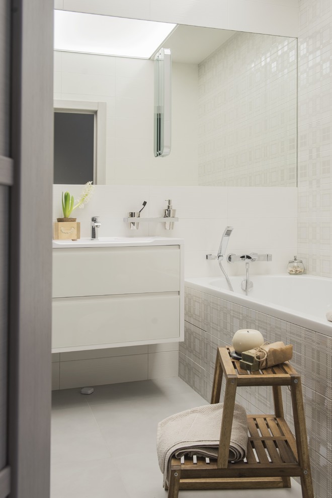 Идея дизайна: маленькая главная ванная комната в современном стиле с плоскими фасадами, белыми фасадами, полновстраиваемой ванной, душем над ванной, белой плиткой, керамогранитной плиткой, белыми стенами, полом из керамогранита, серым полом, шторкой для ванной, зеркалом с подсветкой, тумбой под одну раковину, подвесной тумбой и многоуровневым потолком для на участке и в саду