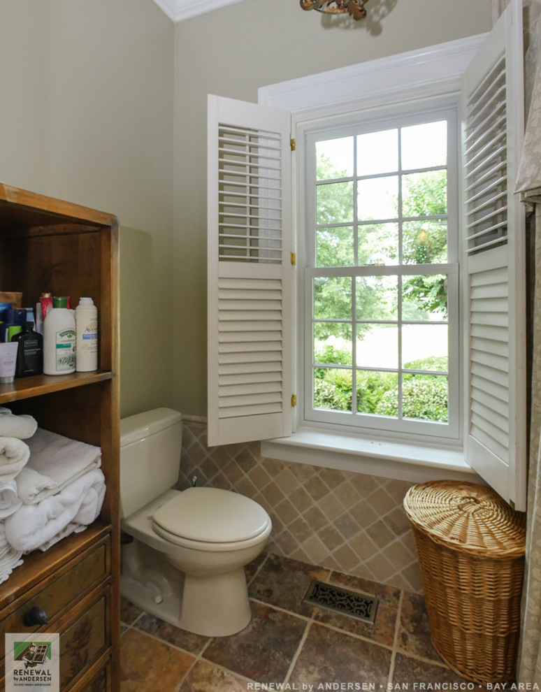 Foto på ett mellanstort beige badrum, med skåp i mellenmörkt trä, ett badkar i en alkov, en dusch/badkar-kombination, en toalettstol med separat cisternkåpa, beige kakel, stenkakel, beige väggar, klinkergolv i keramik, ett undermonterad handfat, bänkskiva i täljsten, brunt golv och dusch med duschdraperi