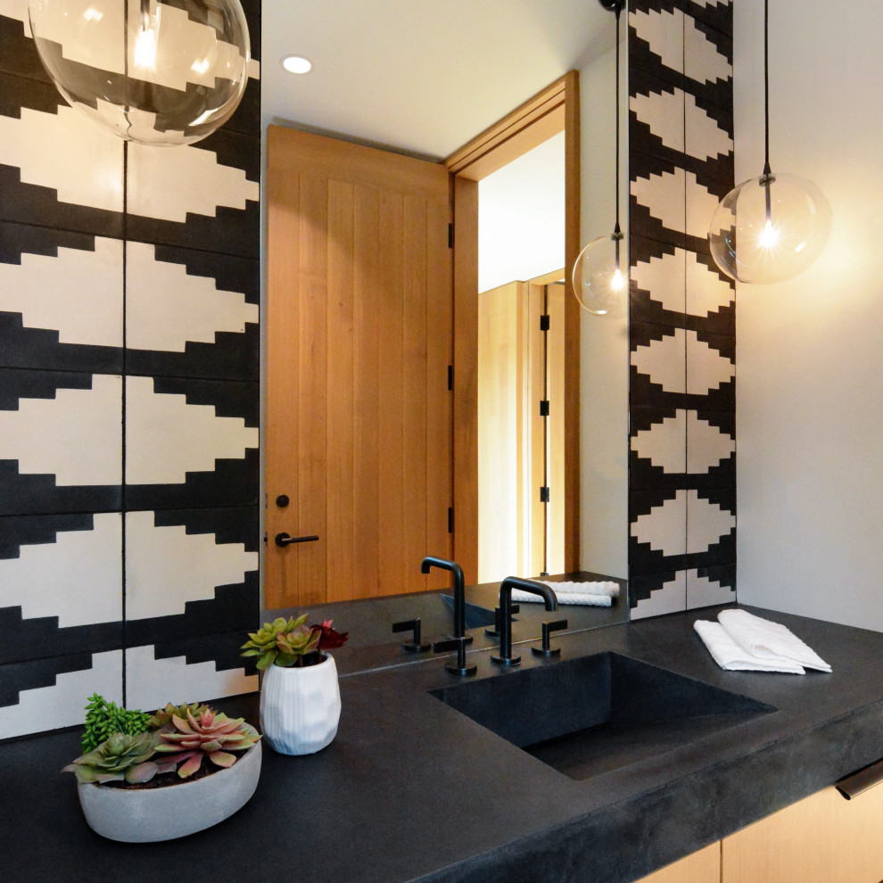 Photo of a large contemporary powder room in Milwaukee with flat-panel cabinets, medium wood cabinets, a one-piece toilet, black and white tile, cement tile, white walls, light hardwood floors, an integrated sink, concrete benchtops, brown floor, black benchtops and a built-in vanity.