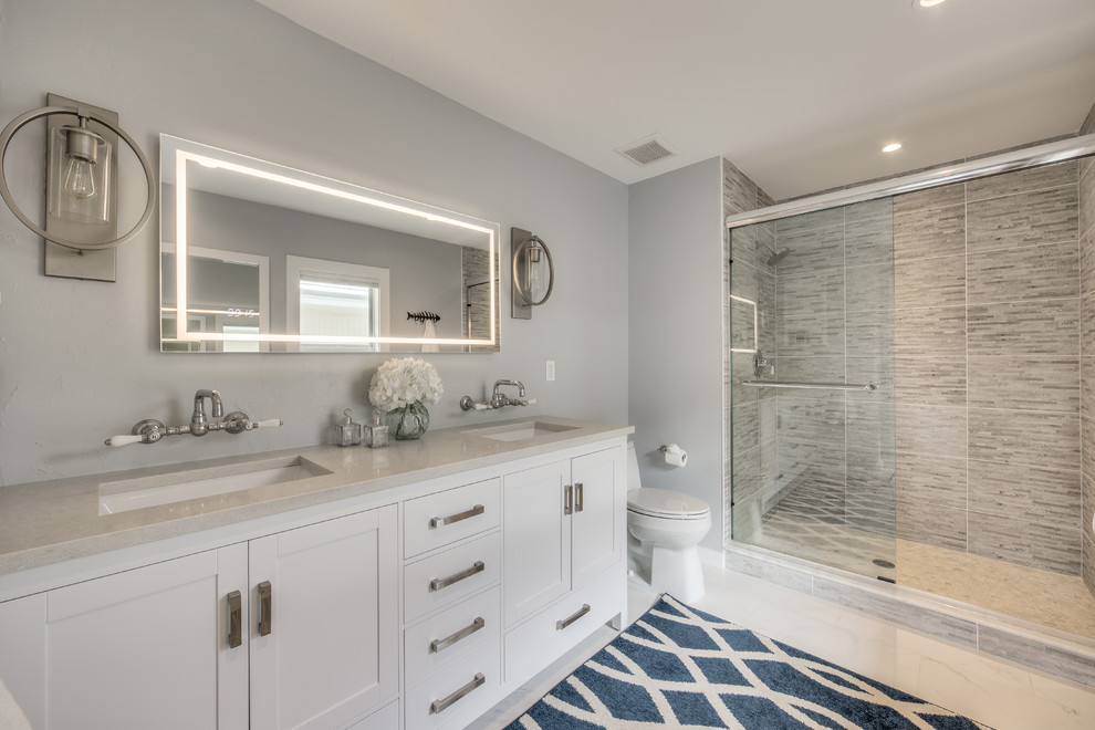 This is an example of a transitional 3/4 bathroom in Philadelphia with shaker cabinets, white cabinets, an alcove shower, a two-piece toilet, gray tile, grey walls, an undermount sink, white floor, a sliding shower screen and beige benchtops.