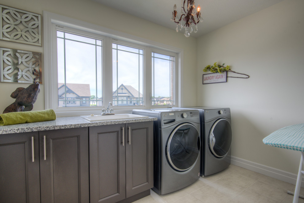 Photo of a mid-sized contemporary single-wall dedicated laundry room in Toronto with a drop-in sink, recessed-panel cabinets, grey cabinets, beige walls, laminate floors, a side-by-side washer and dryer, beige floor and multi-coloured benchtop.