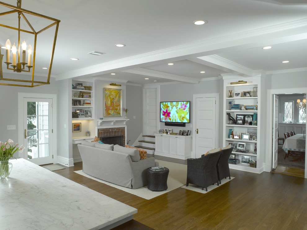This is an example of a transitional open concept family room in New York with medium hardwood floors, grey walls, a standard fireplace, a brick fireplace surround and a wall-mounted tv.