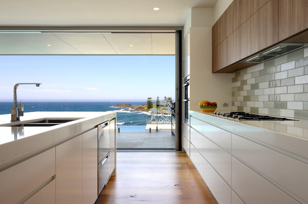 Photo of a mid-sized modern galley eat-in kitchen in Wollongong with a double-bowl sink, flat-panel cabinets, medium wood cabinets, quartz benchtops, grey splashback, terra-cotta splashback, stainless steel appliances, medium hardwood floors and with island.