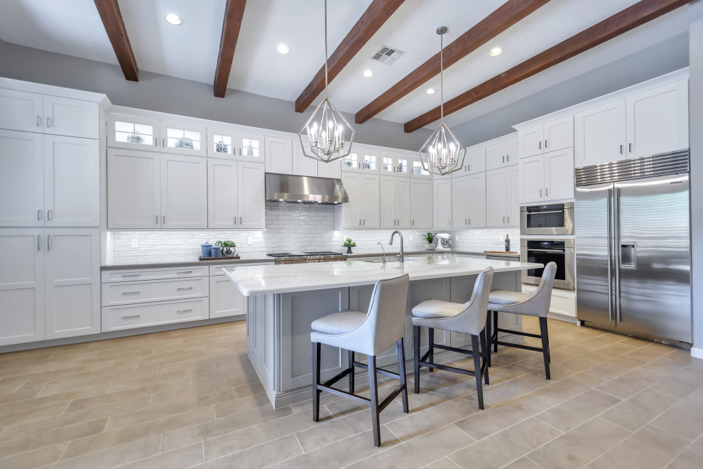 Eat-in kitchen - large transitional l-shaped porcelain tile and brown floor eat-in kitchen idea in Phoenix with a farmhouse sink, shaker cabinets, white cabinets, quartz countertops, white backsplash, subway tile backsplash, stainless steel appliances, an island and gray countertops