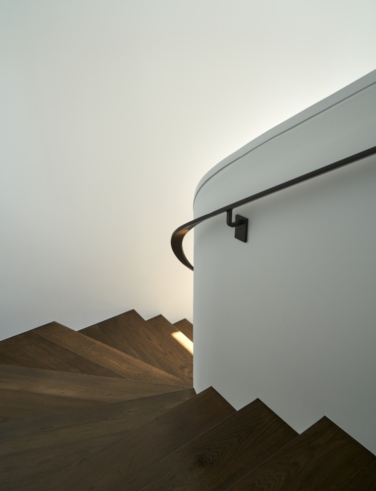 На фото: изогнутая металлическая лестница в современном стиле с деревянными ступенями и перилами из смешанных материалов