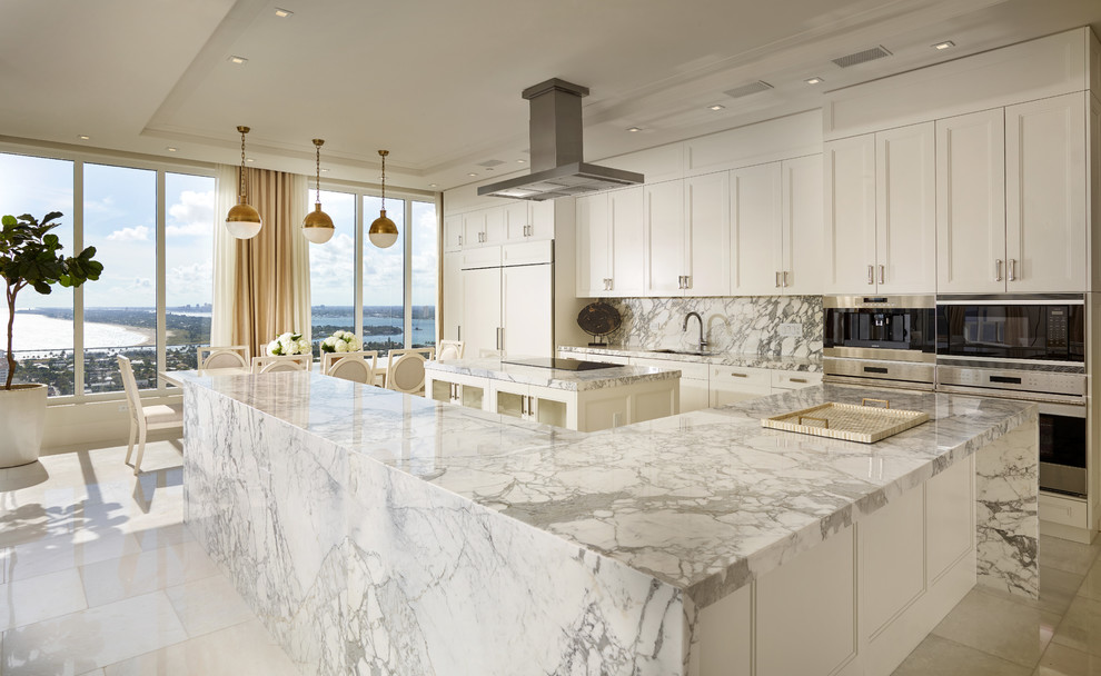 This is an example of a large transitional eat-in kitchen in Miami with an undermount sink, recessed-panel cabinets, white cabinets, marble benchtops, white splashback, stone slab splashback, panelled appliances, marble floors and multiple islands.