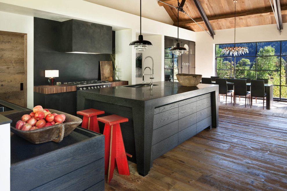 This is an example of a country l-shaped eat-in kitchen in Other with an undermount sink, flat-panel cabinets, black cabinets, black splashback, medium hardwood floors, with island, brown floor and black benchtop.