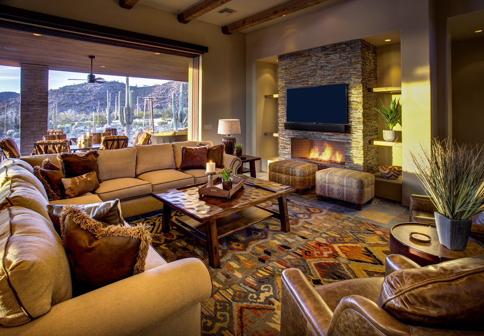 This is an example of a mid-sized open concept family room in Phoenix with beige walls, slate floors, a standard fireplace, a stone fireplace surround, a wall-mounted tv and grey floor.
