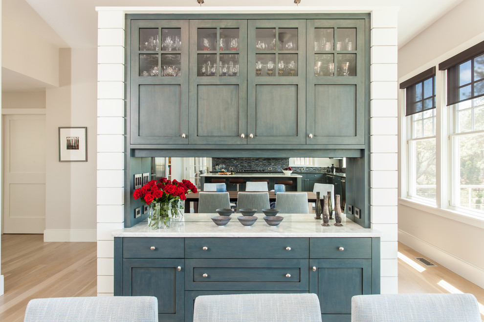 Inspiration for a large beach style l-shaped eat-in kitchen in Boston with an undermount sink, raised-panel cabinets, blue cabinets, marble benchtops, blue splashback, glass tile splashback, stainless steel appliances, light hardwood floors and with island.
