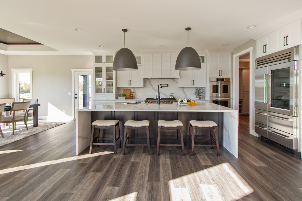 Example of a transitional vinyl floor and brown floor open concept kitchen design with an undermount sink, recessed-panel cabinets, white cabinets, quartz countertops, white backsplash, stone slab backsplash, stainless steel appliances, an island and white countertops