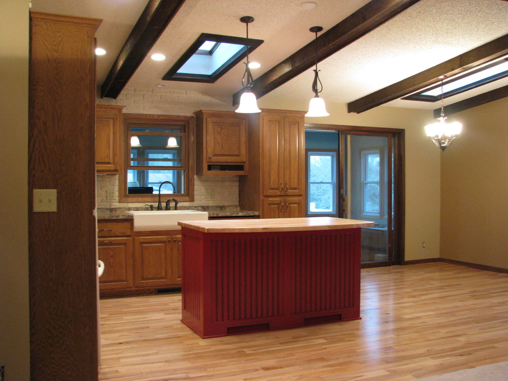 This is an example of a mid-sized country l-shaped eat-in kitchen in Minneapolis with a farmhouse sink, raised-panel cabinets, medium wood cabinets, wood benchtops, grey splashback, stone tile splashback, white appliances, light hardwood floors and with island.