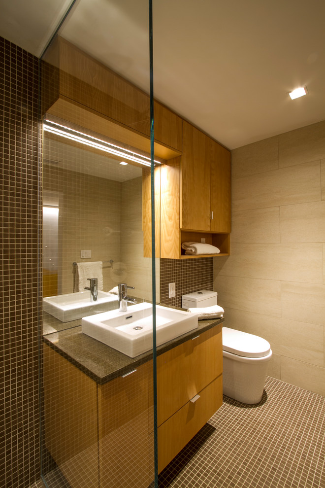 Inspiration for a mid-sized contemporary 3/4 bathroom in New York with flat-panel cabinets, light wood cabinets, a curbless shower, a one-piece toilet, beige tile, porcelain tile, brown walls, pebble tile floors, a vessel sink and quartzite benchtops.