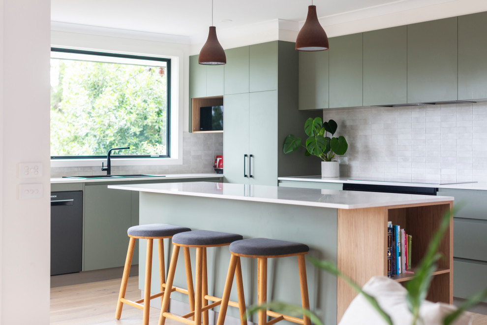 This is an example of a mid-sized contemporary l-shaped open plan kitchen in Canberra - Queanbeyan with a double-bowl sink, flat-panel cabinets, green cabinets, quartz benchtops, white splashback, stone tile splashback, black appliances, medium hardwood floors, with island, beige floor and white benchtop.