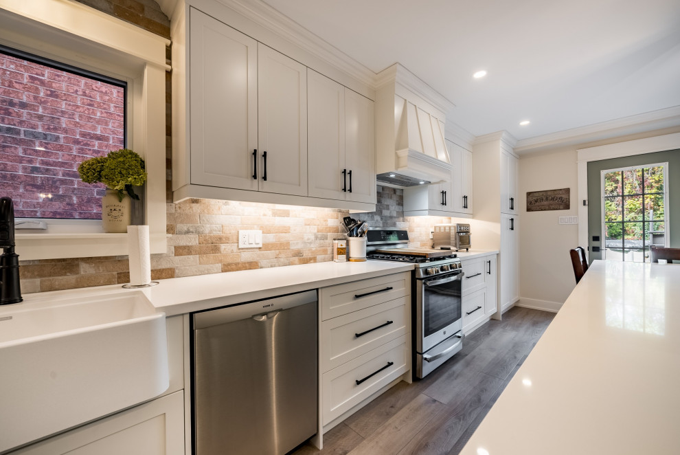 Design ideas for a large country l-shaped eat-in kitchen in DC Metro with a farmhouse sink, shaker cabinets, white cabinets, quartz benchtops, red splashback, brick splashback, stainless steel appliances, medium hardwood floors, with island, yellow floor and white benchtop.