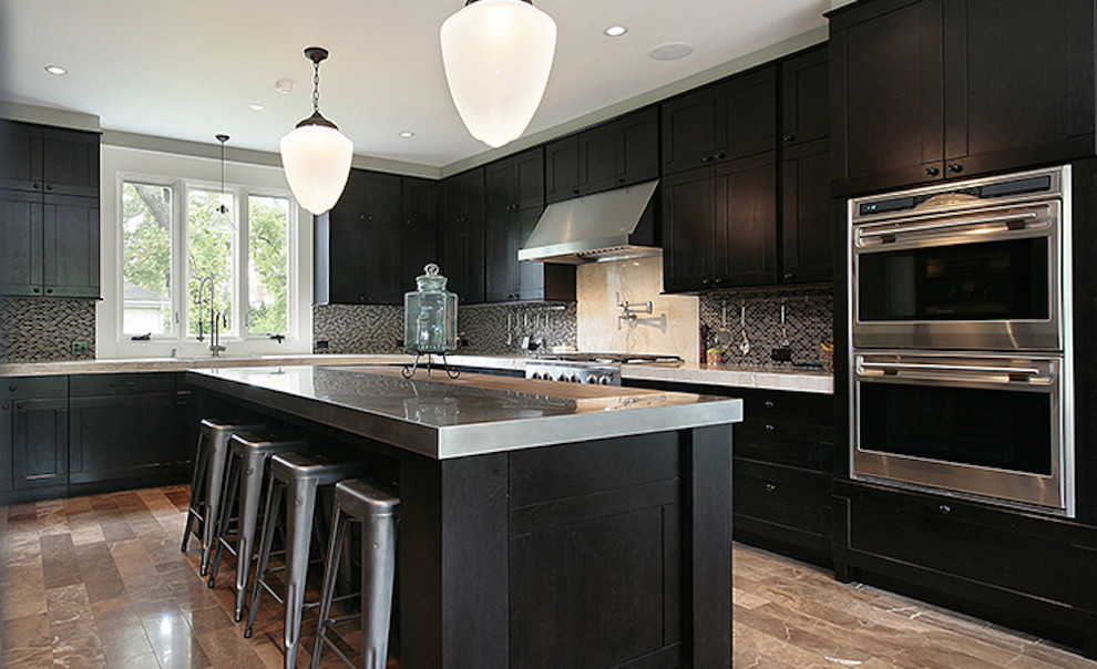 Photo of a kitchen in New Orleans with a drop-in sink, dark wood cabinets, stainless steel benchtops, brown splashback, mosaic tile splashback, stainless steel appliances and with island.