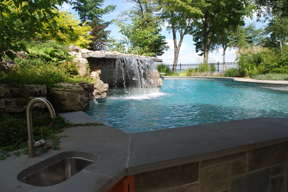 Large beach style backyard custom-shaped natural pool in Montreal with a water feature and natural stone pavers.