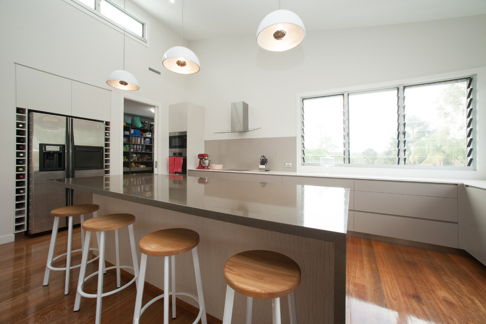 Photo of a contemporary l-shaped eat-in kitchen in Brisbane with an undermount sink, flat-panel cabinets, beige cabinets, quartz benchtops, beige splashback, glass sheet splashback, stainless steel appliances, medium hardwood floors and with island.