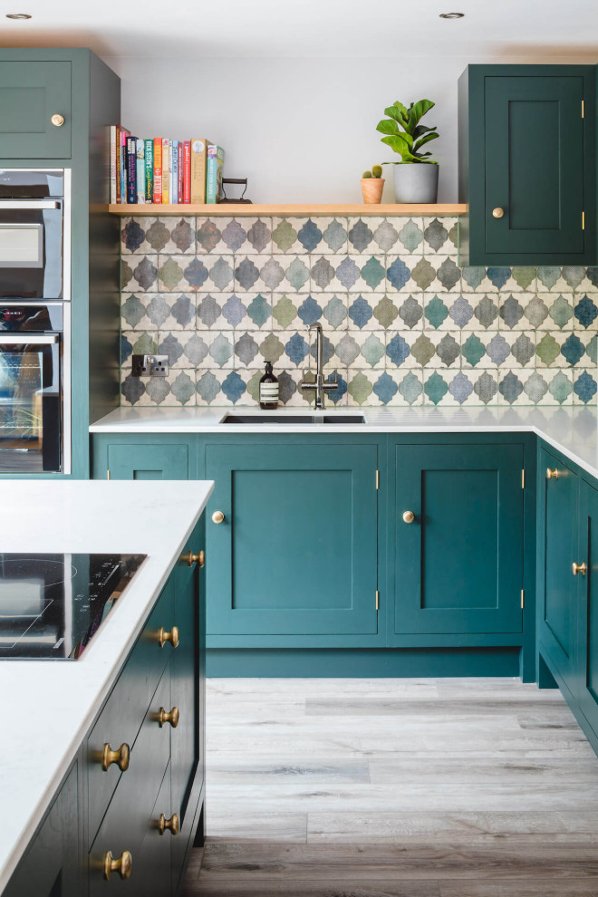 This is an example of a mid-sized contemporary l-shaped eat-in kitchen in Other with a drop-in sink, shaker cabinets, green cabinets, quartzite benchtops, green splashback, ceramic splashback, laminate floors, with island and white benchtop.