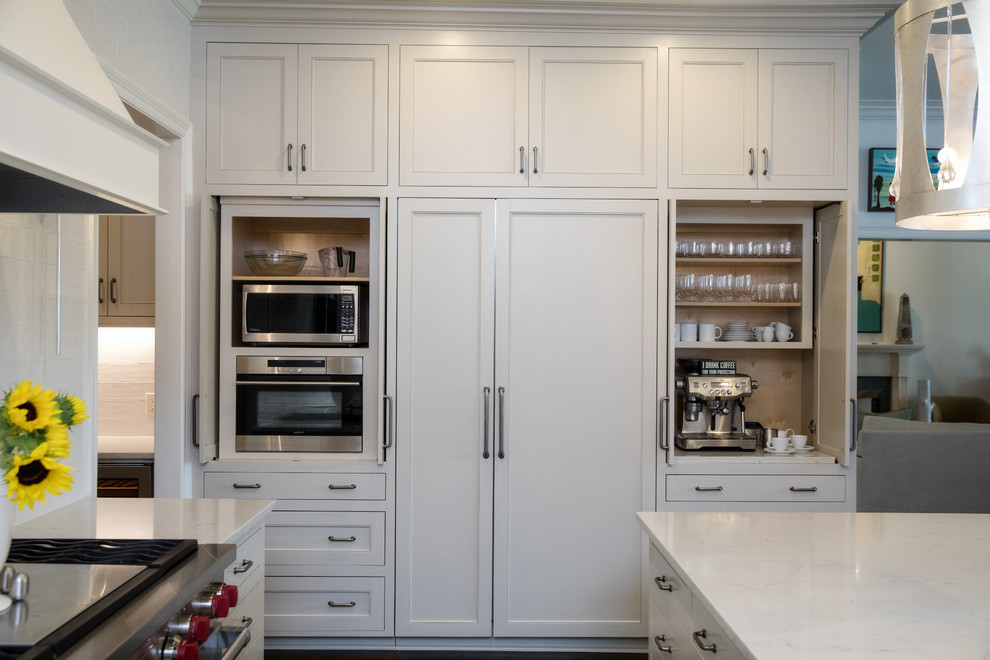 This is an example of a transitional l-shaped kitchen pantry in New Orleans with a single-bowl sink, shaker cabinets, white cabinets, quartz benchtops, white splashback, stainless steel appliances, with island and white benchtop.