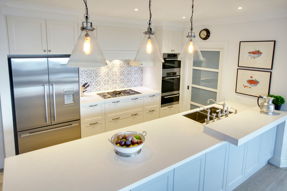 Photo of a large beach style single-wall kitchen pantry in Melbourne with a double-bowl sink, beaded inset cabinets, white cabinets, solid surface benchtops, mosaic tile splashback, stainless steel appliances, plywood floors and with island.