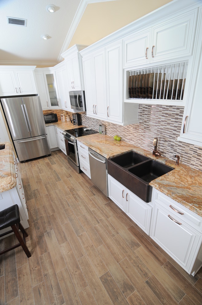 Example of a transitional medium tone wood floor kitchen design in Miami with a farmhouse sink, raised-panel cabinets, white cabinets, granite countertops, multicolored backsplash, ceramic backsplash, stainless steel appliances and an island