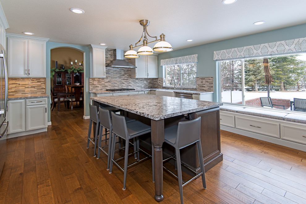 Large transitional medium tone wood floor enclosed kitchen photo with a farmhouse sink, recessed-panel cabinets, white cabinets, granite countertops, multicolored backsplash, matchstick tile backsplash, stainless steel appliances and an island