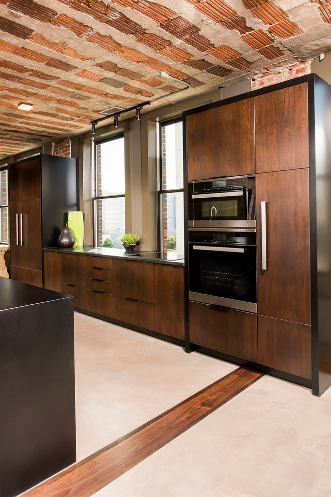 This is an example of a large industrial galley kitchen pantry in Raleigh with an undermount sink, flat-panel cabinets, dark wood cabinets, granite benchtops, panelled appliances, concrete floors, multiple islands and beige floor.