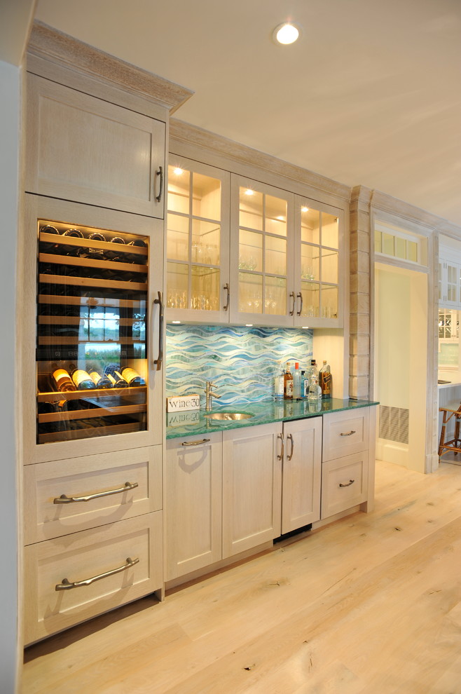 Photo of a mid-sized beach style single-wall wet bar in New York with an undermount sink, shaker cabinets, light wood cabinets, glass benchtops, blue splashback, ceramic splashback, light hardwood floors, brown floor and turquoise benchtop.