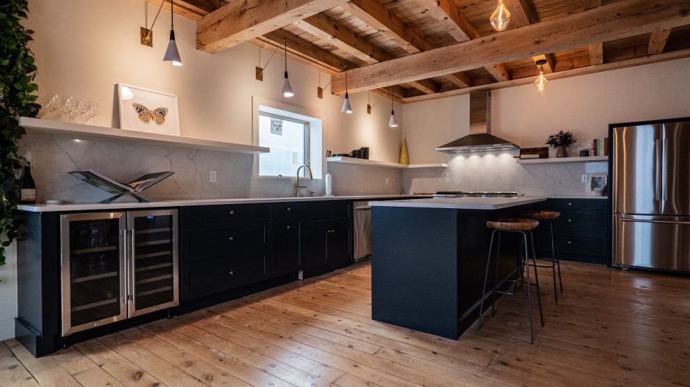 Mid-sized contemporary l-shaped eat-in kitchen in New York with an undermount sink, flat-panel cabinets, black cabinets, quartzite benchtops, white splashback, stone slab splashback, stainless steel appliances, medium hardwood floors, with island, brown floor, white benchtop and exposed beam.