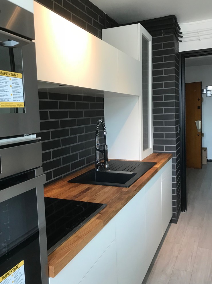 Small contemporary galley separate kitchen in Reims with a single-bowl sink, white cabinets, wood benchtops, black splashback, brick splashback, stainless steel appliances and no island.