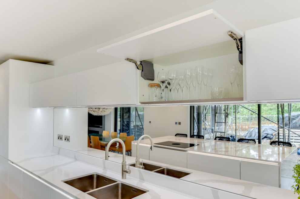 This is an example of a large modern single-wall eat-in kitchen in Sussex with a double-bowl sink, flat-panel cabinets, white cabinets, quartzite benchtops, multi-coloured splashback, mirror splashback, black appliances, porcelain floors, with island, grey floor and white benchtop.