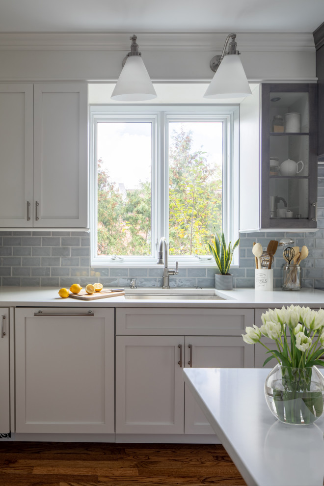 Inspiration for a mid-sized transitional l-shaped medium tone wood floor and brown floor enclosed kitchen remodel with an undermount sink, shaker cabinets, white cabinets, quartz countertops, blue backsplash, subway tile backsplash, stainless steel appliances, an island and white countertops