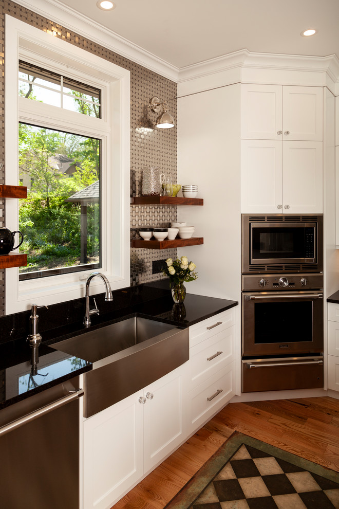 Mid-sized transitional l-shaped enclosed kitchen photo with shaker cabinets, white cabinets, stainless steel appliances, an island and black countertops