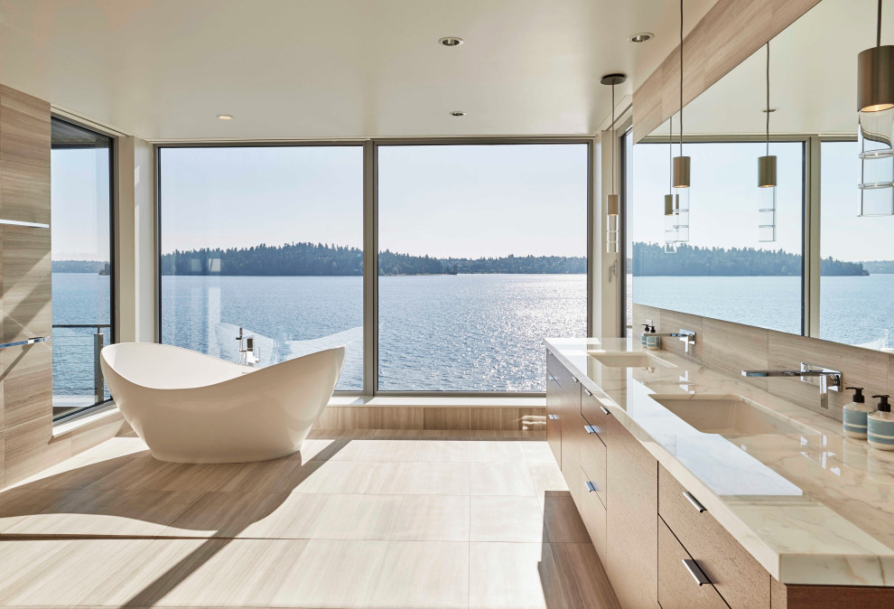 This is an example of a large contemporary master bathroom in Seattle with flat-panel cabinets, medium wood cabinets, a freestanding tub, beige tile, porcelain tile, porcelain floors, an undermount sink, limestone benchtops, beige floor and beige benchtops.