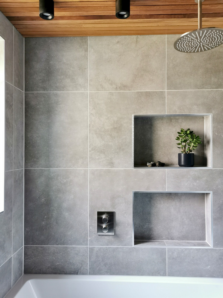 This is an example of a small contemporary bathroom in Other with flat-panel cabinets, brown cabinets, a drop-in tub, a shower/bathtub combo, a wall-mount toilet, gray tile, porcelain tile, grey walls, porcelain floors, grey floor, a single vanity, a floating vanity and timber.