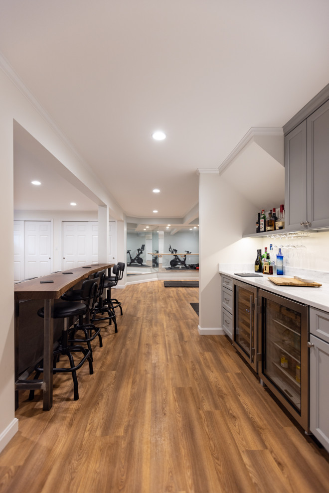 Photo of a medium sized modern basement in Boston with a home bar, grey walls, vinyl flooring, a ribbon fireplace and brown floors.