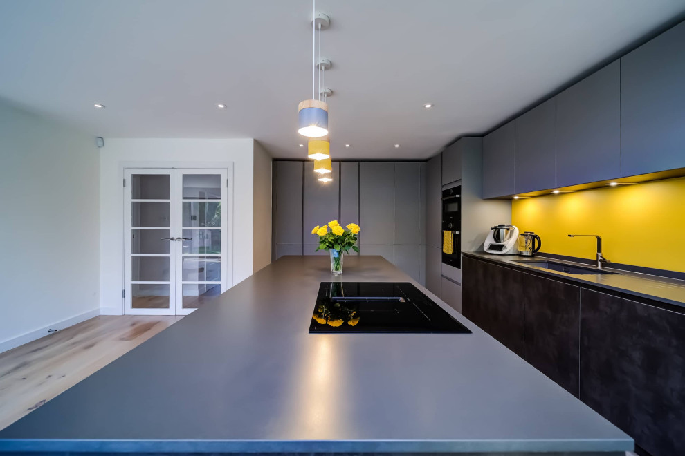 Design ideas for a large modern l-shaped open plan kitchen in London with flat-panel cabinets, grey cabinets, engineered stone countertops, yellow splashback, black appliances, an island and grey worktops.