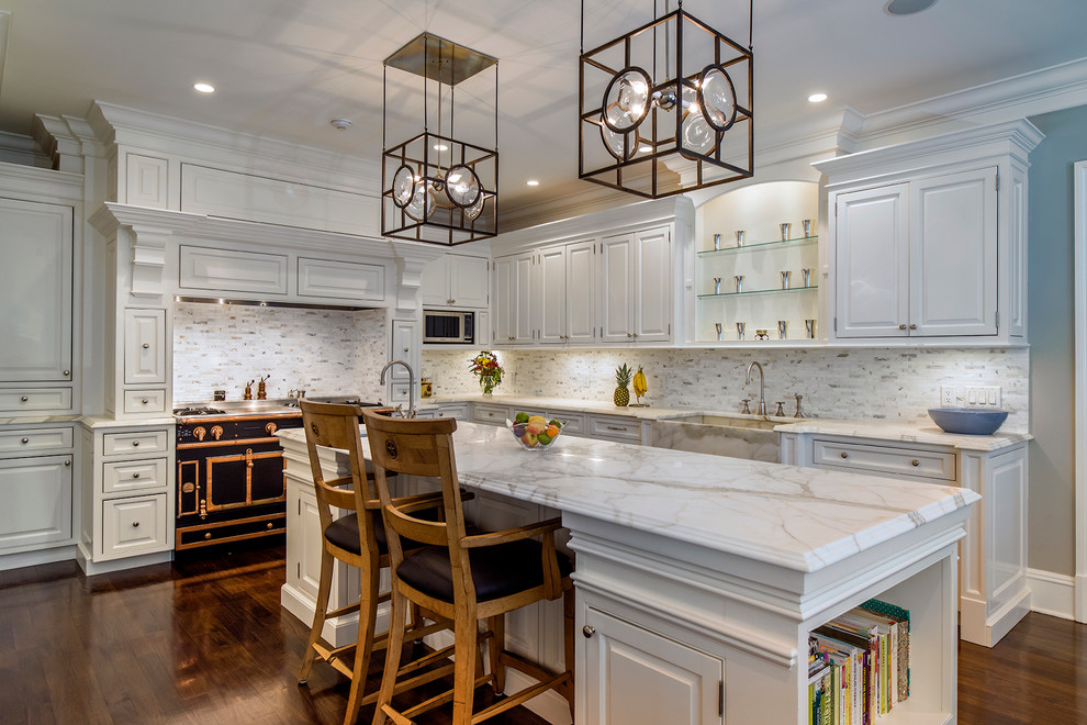 Photo of a traditional l-shaped kitchen in New York with a farmhouse sink, raised-panel cabinets, white cabinets, white splashback, black appliances, dark hardwood floors, with island and marble benchtops.