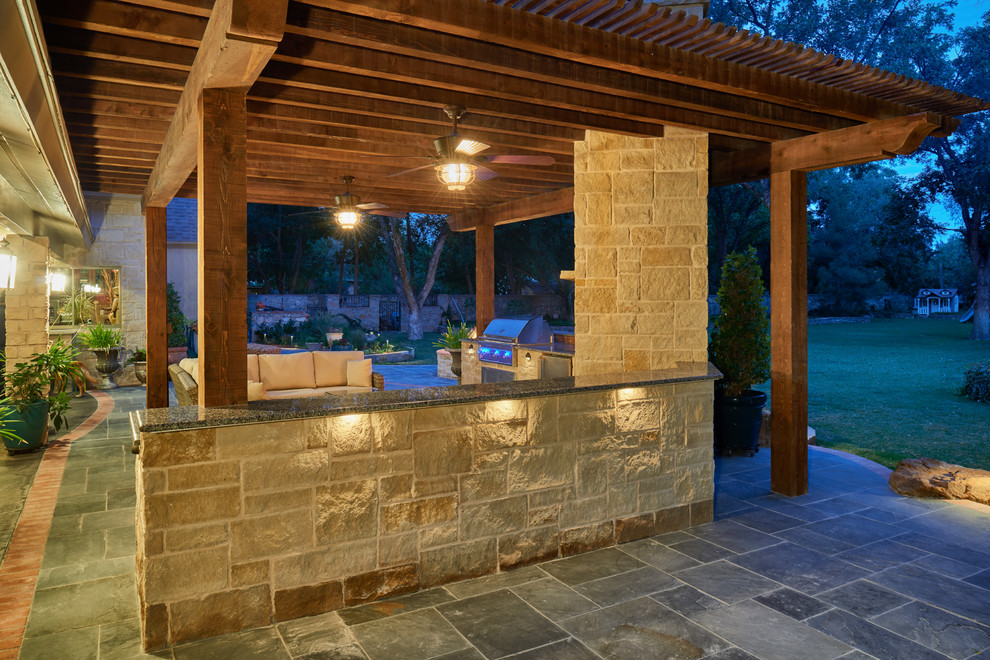 This is an example of a traditional backyard patio in Austin with an outdoor kitchen, natural stone pavers and a pergola.