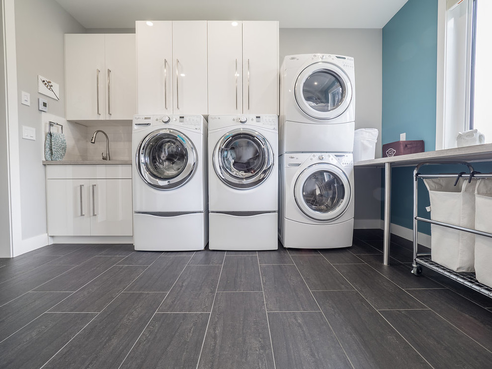 Design ideas for a large modern l-shaped dedicated laundry room in Edmonton with a double-bowl sink, flat-panel cabinets, white cabinets, solid surface benchtops, blue walls, porcelain floors, a side-by-side washer and dryer and grey floor.