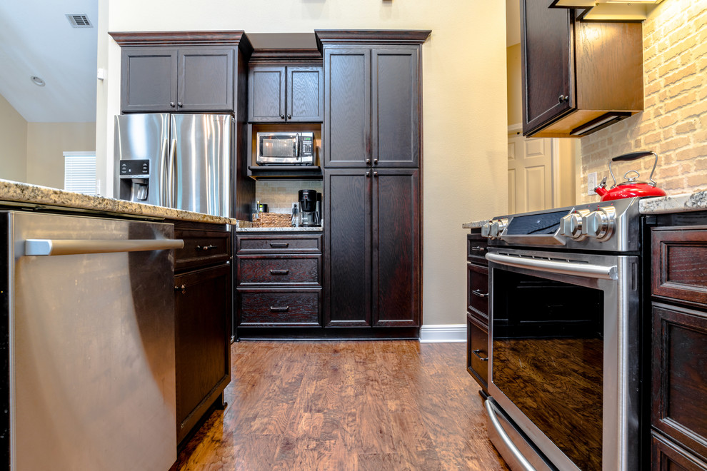 Large transitional l-shaped vinyl floor eat-in kitchen photo in Miami with an undermount sink, shaker cabinets, dark wood cabinets, granite countertops, beige backsplash, porcelain backsplash, stainless steel appliances and an island