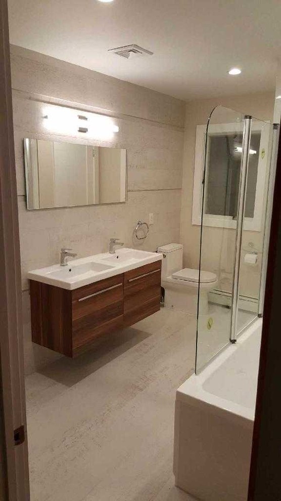 Inspiration for a mid-sized contemporary master bathroom in New York with flat-panel cabinets, dark wood cabinets, an alcove tub, a shower/bathtub combo, a one-piece toilet, beige tile, beige walls, light hardwood floors, an integrated sink, quartzite benchtops, beige floor and a hinged shower door.