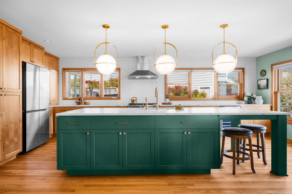 Example of a transitional l-shaped medium tone wood floor and brown floor kitchen design with shaker cabinets, white backsplash, an island, white countertops, an undermount sink, medium tone wood cabinets and stainless steel appliances