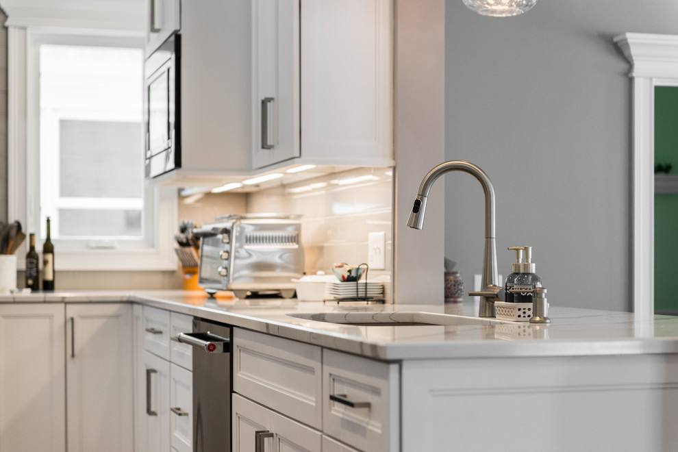 Inspiration for a mid-sized transitional l-shaped medium tone wood floor and brown floor eat-in kitchen remodel in Chicago with an undermount sink, recessed-panel cabinets, white cabinets, quartzite countertops, gray backsplash, subway tile backsplash, black appliances, no island and multicolored countertops